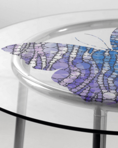Dettaglio di tavolo in vetro con stampa digitale di farfalla stilizzata nei toni del blu e viola.